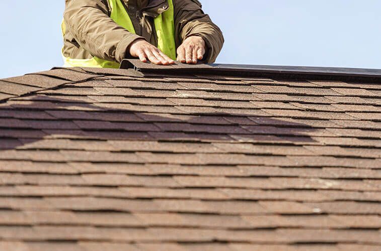 A man is working on a roof with shingles.